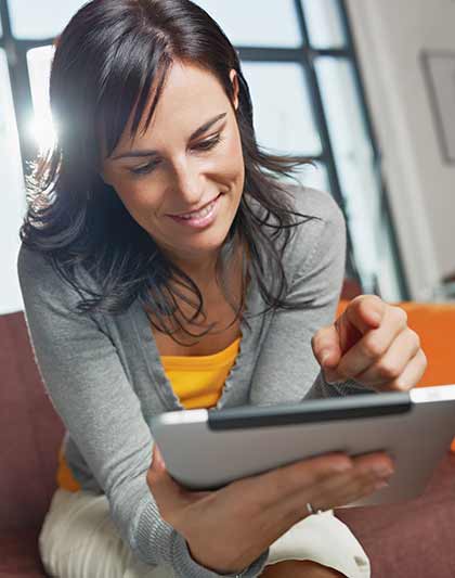 Junge Frau mit dunklem Haar bedient lächelnd ein Tablet.