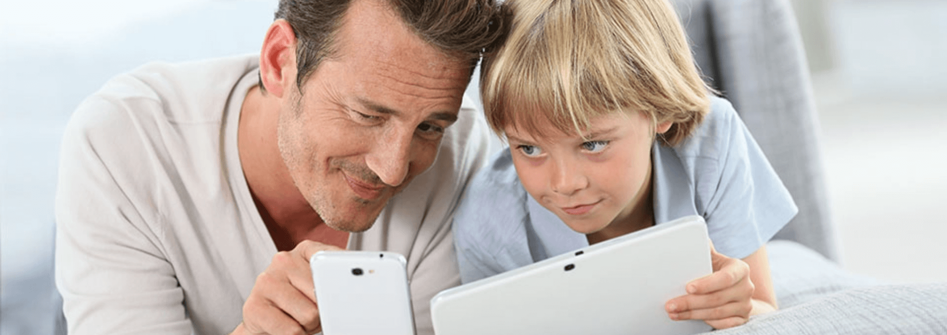Vater und Sohn lesen das ePaper. Der Junge hält das Tablet und der Vater ein Smartphone. Beide schauen auf das Smartphone.